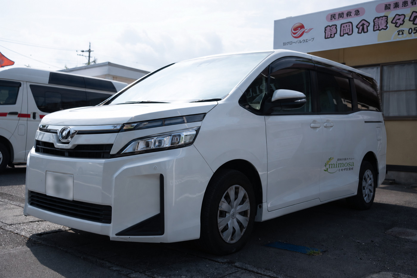 静岡介護タクシーの看板の前に停めたミモザ営業所の福祉車両